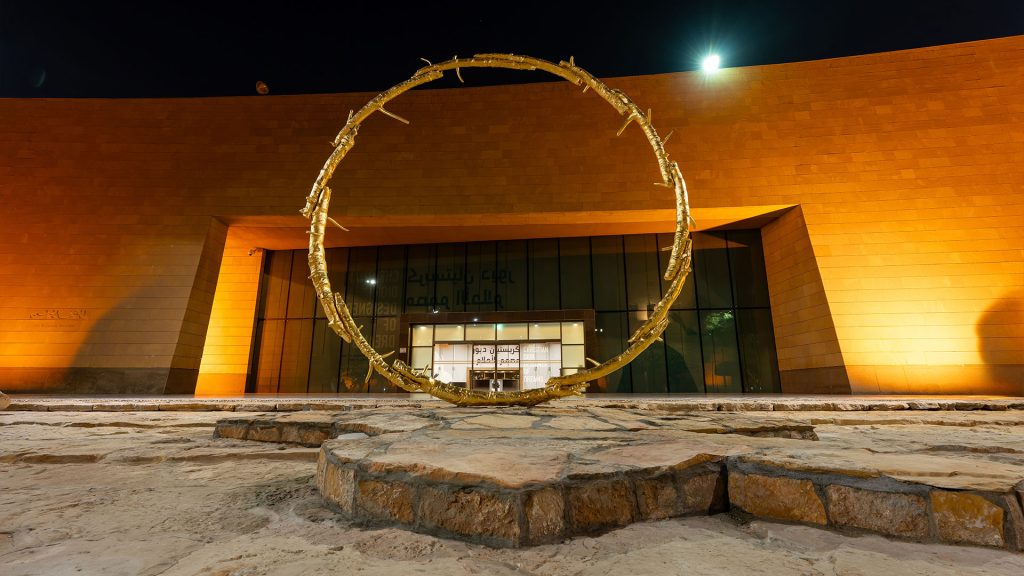 A large, bright yellow circular sculpture by Ugo Rondinone, titled the sun, installed in an open public space in Riyadh.
