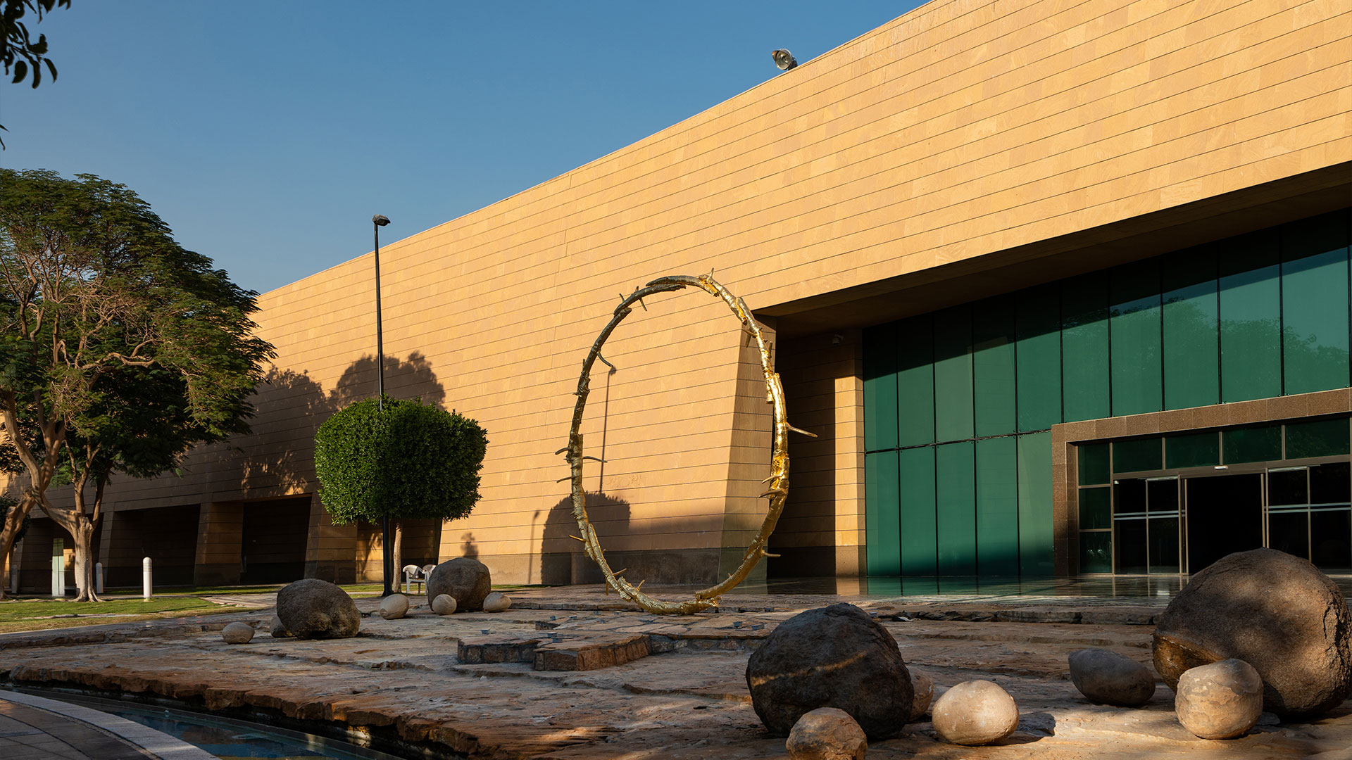 A large, bright yellow circular sculpture by Ugo Rondinone, titled the sun, installed in an open public space in Riyadh.