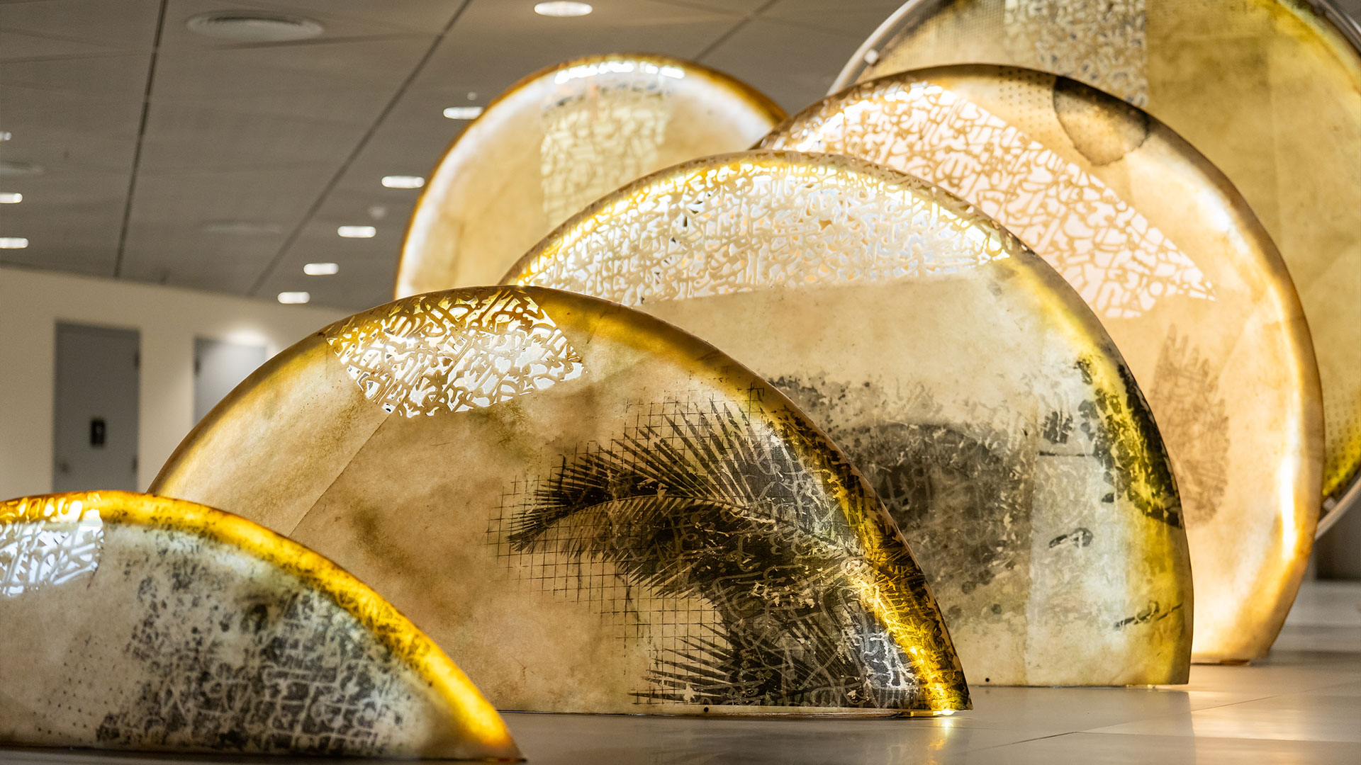 A poetic mixed media installation by Zaman Jassim, titled When the Moon is Full, featuring holographic light, Arabic calligraphy, and layered visual elements evoking memory and departure.