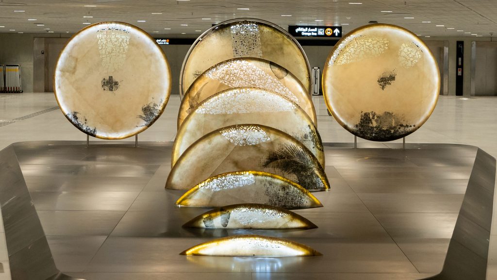 A poetic mixed media installation by Zaman Jassim, titled When the Moon is Full, featuring holographic light, Arabic calligraphy, and layered visual elements evoking memory and departure.