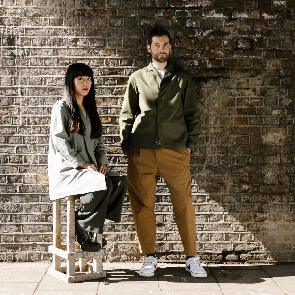 Portrait of artist duo A.A.Murakami—Alexander Groves and Azusa Murakami—standing together in a minimal studio setting, surrounded by ethereal materials and equipment used in their sensory installations.