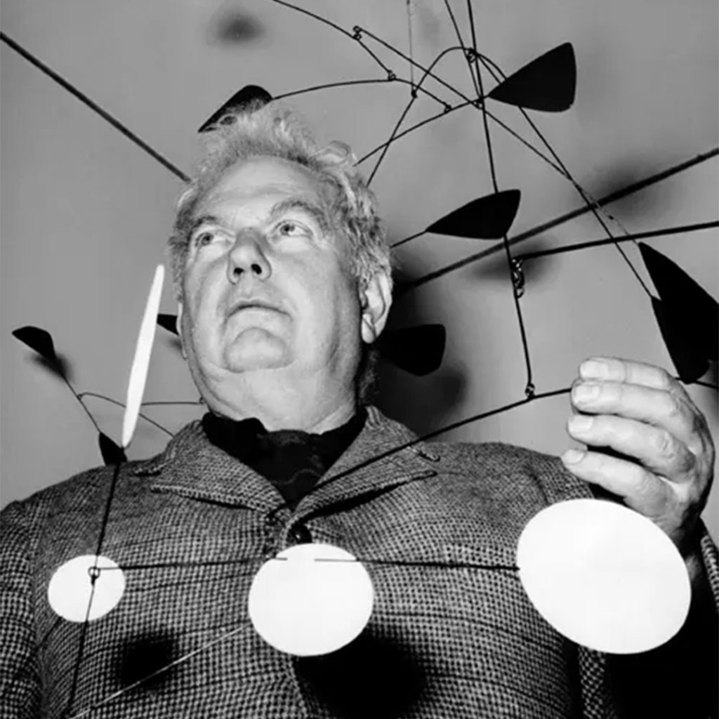 Portrait of Alexander Calder (b. 1898), American sculptor and inventor of the mobile, standing beside one of his large-scale kinetic artworks. Known for his colorful, dynamic compositions that blend engineering and abstraction.