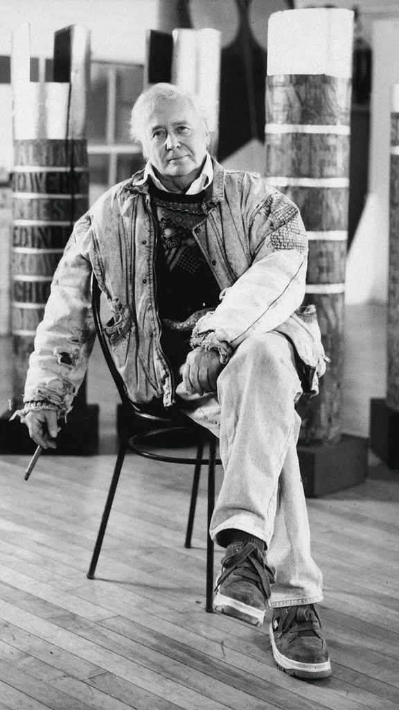 Black-and-white portrait of Robert Indiana (b. 1928), American artist known for his bold typographic works and Pop art legacy, seated in his Coenties Slip studio.